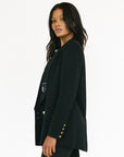 Woman wearing a black blazer with gold buttons on a white background