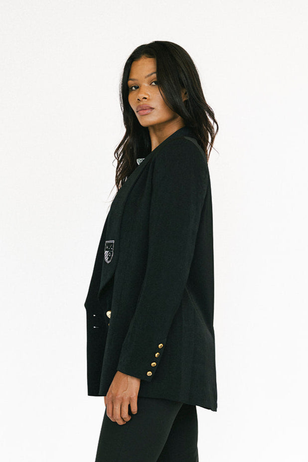 Woman wearing a black blazer with gold buttons on a white background