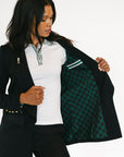 Woman wearing a black blazer with green and white checkered lining, white shirt, and black pants.