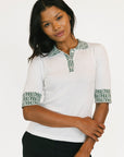 stylish women’s golf top outfit. Woman wearing a white blouse with green patterned accents on a plain background