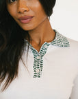 Woman wearing a white blouse with green patterned collar against a plain background