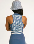 Woman wearing a blue sleeveless top and skirt with a patterned cap on a white background