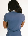 Woman wearing a blue polo with white accents on a plain background