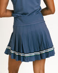 Blue pleated skirt with white and green trim worn by a person on a plain background