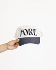 Cap with 'FORE' text held by a hand on a white background