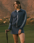 Woman in a blue tracksuit standing on a golf course with mountains in the background