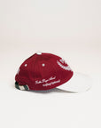 A person wearing a burgundy and white baseball cap with text and leaf patterns.