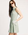Woman wearing a light green dress and sunglasses on a plain background
