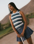 Woman in a striped sleeveless top and blue skirt holding a golf club with a golf course in the background