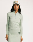 Woman wearing a light green long-sleeve dress and cap on a white background
