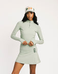 Woman wearing a light green long-sleeve top and skirt with a matching cap on a white background