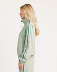 Woman wearing a light green jacket with a high collar and white pants on a white background