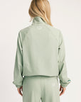 Person wearing a light green tracksuit with a brand logo on a white background
