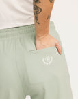 Light green sweatpants with a logo on the pocket worn by a person with tattoos.