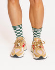 Person wearing green and white checkered socks with tan sneakers on a plain background