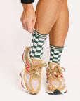 Person wearing green checkered socks with beige sneakers on a white background