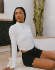 A woman wearing a white long sleeve golf top with a mock neckline.