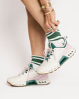 White sneakers with green accents worn by a person on a light gray background