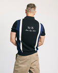 A man wearing a navy zip sweater with vertical white stripes and the text 'Fore All' on the chest, paired with beige pants.