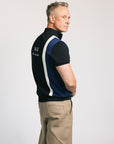A man wearing a navy zip sweater with vertical white stripes and the text 'Fore All' on the chest, paired with beige pants.