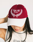 A person wearing a burgundy and white baseball cap with text and leaf patterns.