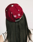 A person wearing a burgundy and white baseball cap with text and leaf patterns.