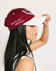 A person wearing a burgundy and white baseball cap with text and leaf patterns.