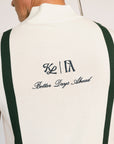 A man wearing a beige zip sweater with vertical green stripes and the text 'Fore All x Khalhon' on the chest, paired with dark green shorts.