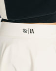 A person wearing an off-white high-waisted skirt with built-in shorts, a black and blue top with the text 'Fore All' on it, and a metal ring detail at the waist.