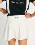 A person wearing an off-white high-waisted skirt with built-in shorts, a black and blue top with the text 'Fore All' on it, and a metal ring detail at the waist.