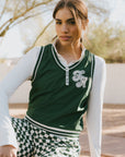 A woman wearing a green sleeveless windbreaker vest with a collar, featuring a white appliquéd logo on the left chest and silicone logos on the upper back.