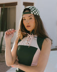 A female model wearing a sleeveless green and pink colorblocked mock neck top with mesh accents and a flat drawstring cord.