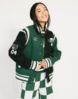 Person wearing a green and black varsity jacket with white accents on a plain background