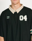 Person wearing a black sports jersey with white lettering and green shorts on a white background