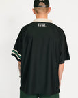 Person wearing a black sports jersey with white lettering and green shorts on a white background