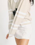 Person wearing a beige cardigan with white stripes over a white dress on a plain background