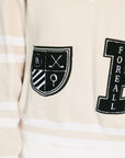 Close-up of a beige sweater with black and white emblem and text