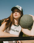 A female model wearing a white sleeveless tank top with a green and pink stripe at the neckline and armholes, and the text 'Chasing Balls' on the chest