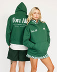 Two people wearing green hoodies with 'Fore All' text on a white background