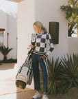 A woman wearing a sleeveless, checkered indigo and white sweater with a mock neck.