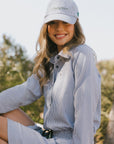 Woman wearing a blue and white striped shirt and cap outdoors with trees in the background
