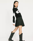 Woman wearing a black and white sweater with a logo, black skirt, and black boots on a white background