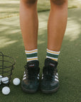A person wearing retro ankle socks in mustard and green colors, paired with a black shoe.