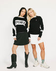 Two women wearing black and white sweaters with visible branding on a white background