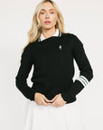 Woman wearing a black dorothy sweater with a white collar and white skirt on a light background