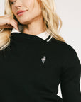 Woman wearing a black dorothy sweater with a white collar and white skirt on a light background