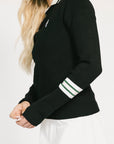 Woman wearing a black dorothy sweater with a white collar and white skirt on a light background