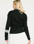 Woman wearing a black dorothy sweater with a white collar and white skirt on a light background