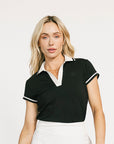 Woman wearing a black polo shirt, white skirt, and sneakers on a white background