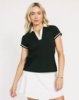 Woman wearing a black and white polo shirt with a white skirt on a plain background